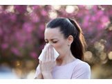 A woman standing in front of trees holds a tissue to her nose
